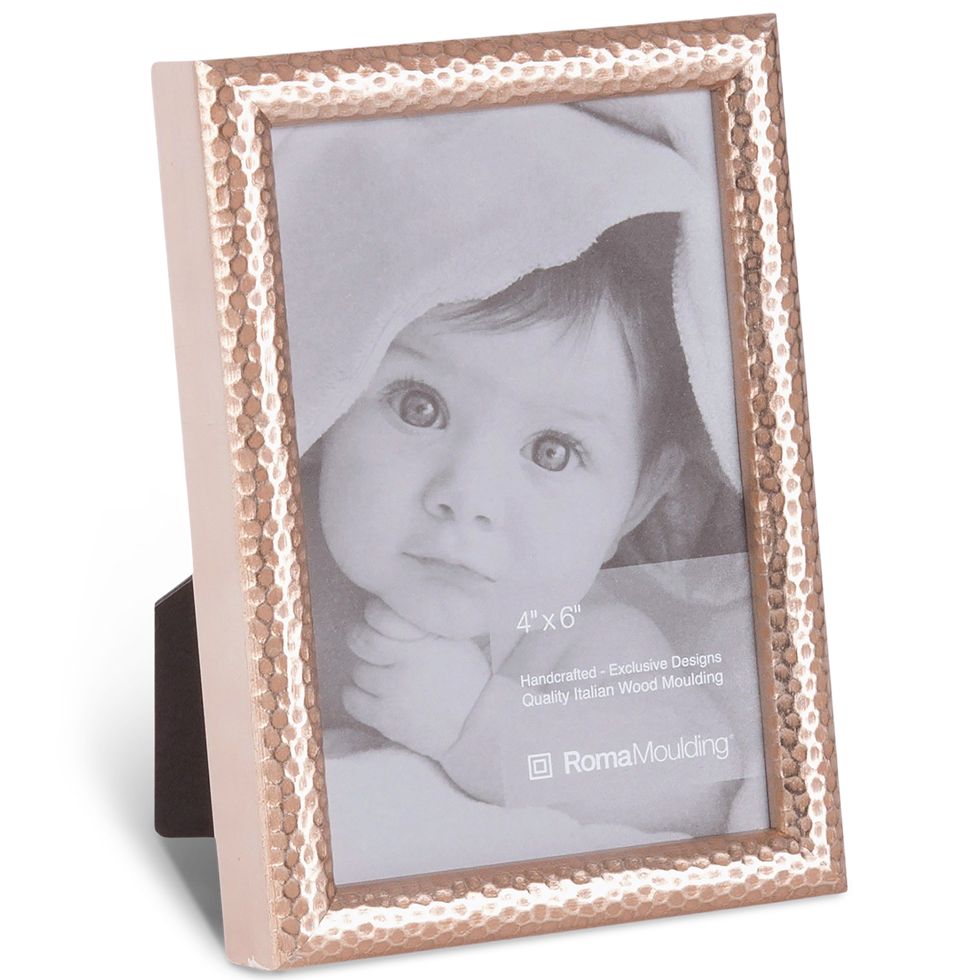 A hammered metal photo frame holds a black-and-white image of an infant with wide eyes, partially covered by a blanket, conveying innocence and warmth.