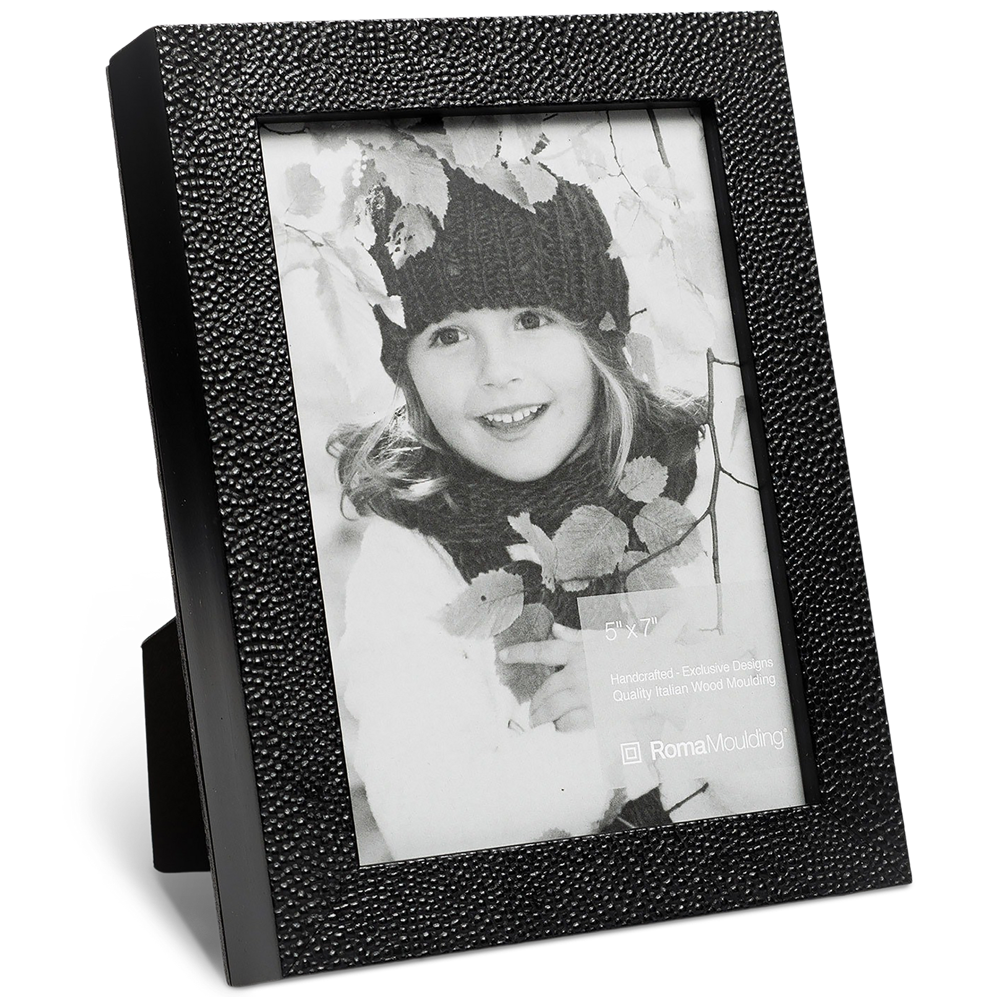Black and white photo of a smiling child in a knit hat, surrounded by leaves, in a textured black picture frame. Warm, nostalgic tone.