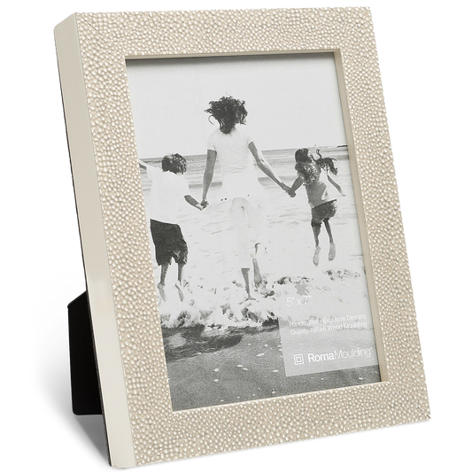 Beige picture frame with a textured border holds a black-and-white photo of three people joyfully running towards the ocean waves, conveying happiness.
