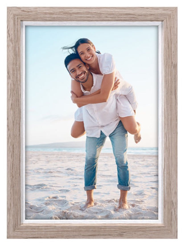 A smiling couple in casual attire enjoys a playful piggyback on a sunny beach, framed in a rustic wooden border, conveying joy and warmth.