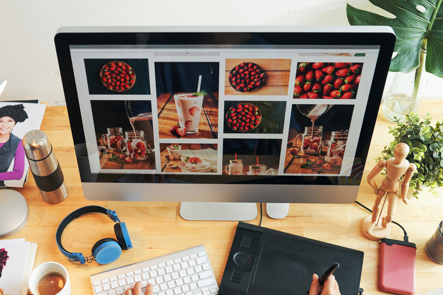 Computer screen displays images of strawberries and drinks; desk items like headphones, a plant, and keyboard surround it, creating a creative workspace.