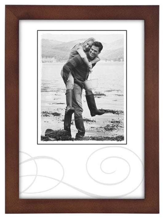 A black-and-white photo in a brown frame shows a smiling couple outdoors. The woman playfully rides on the man's back near a scenic lake shore.