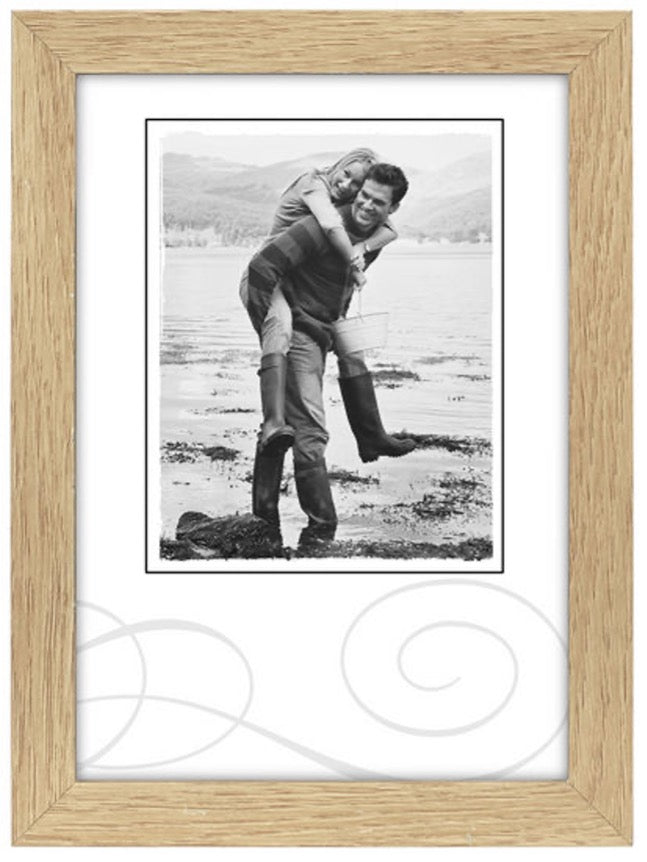 A black-and-white photo of a smiling couple by a lake, with one person giving the other a piggyback ride. They're wearing boots. The mood is joyful.