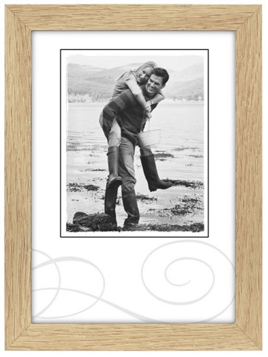 A black-and-white photo of a smiling couple by a lake, with one person giving the other a piggyback ride. They're wearing boots. The mood is joyful.