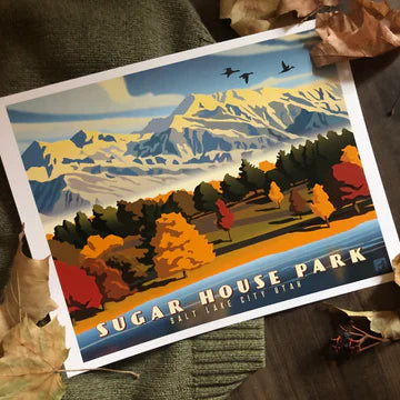 A vibrant print of Sugar House Park, Salt Lake City, showing colorful autumn trees against snow-capped mountains. Fallen leaves and a sweater add a cozy feel.