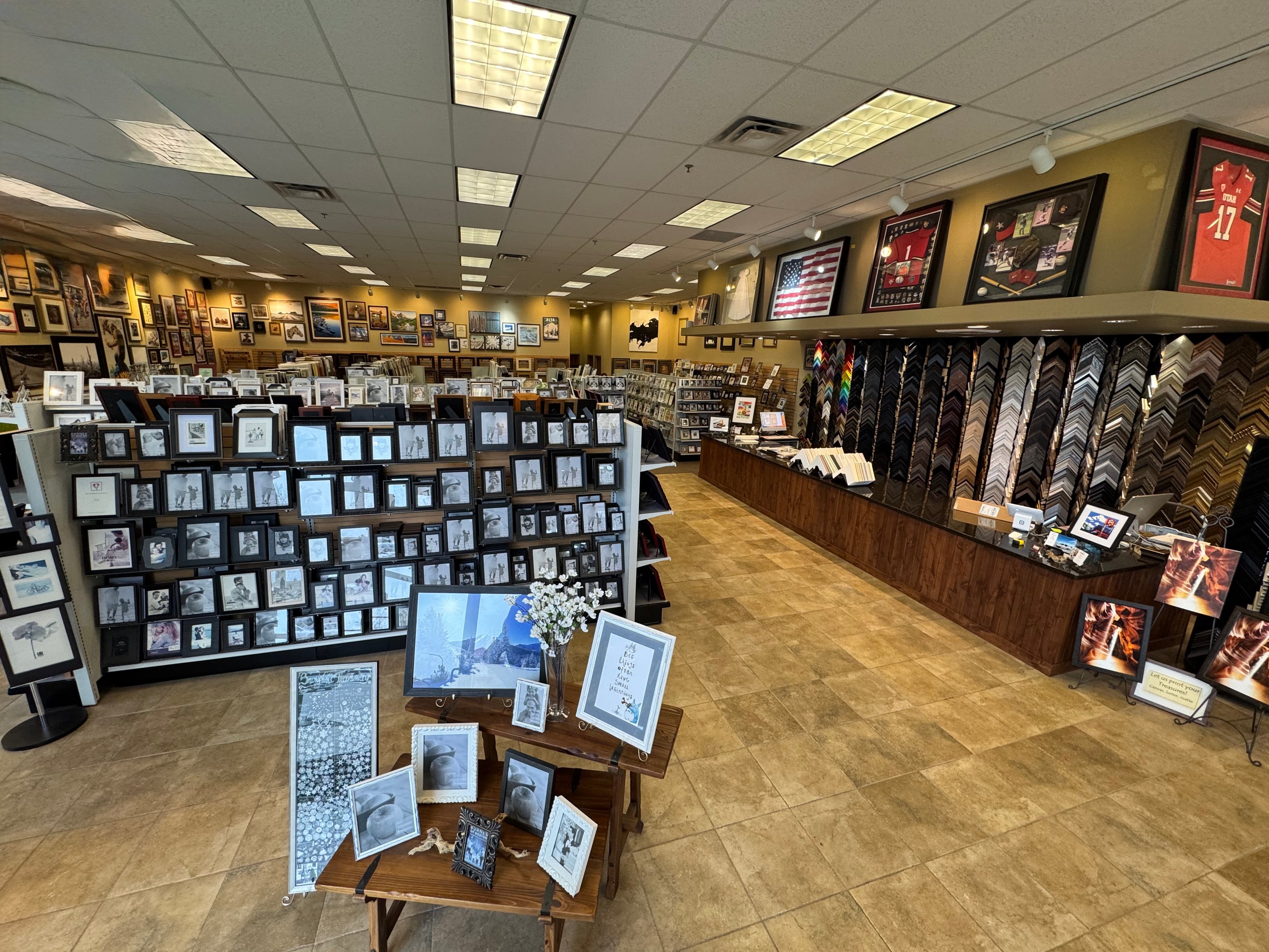 Interior of a store with various framed pictures and photo albums on shelves and display tables.