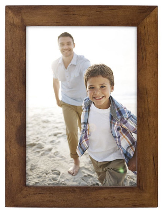 Young boy and man joyfully run on a sunny beach, captured in a wooden frame. The scene conveys happiness and warmth, evoking a sense of carefree summer fun.