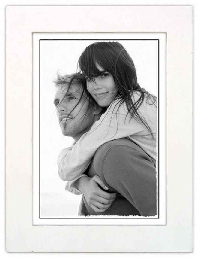 Black and white photo of a woman playfully piggybacking on a man, her hair blowing in the wind. The image radiates joy and captures a carefree moment.