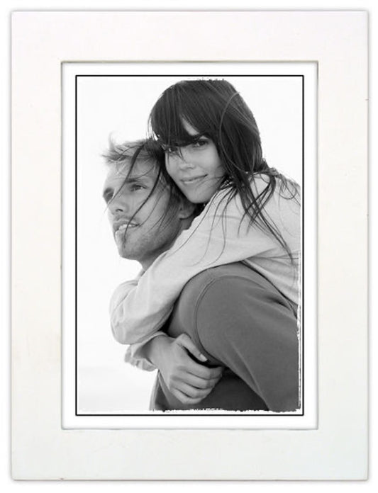Black and white photo of a woman playfully piggybacking on a man, her hair blowing in the wind. The image radiates joy and captures a carefree moment.