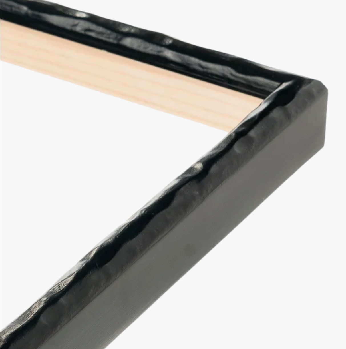Close-up of a picture frame corner with a textured black edge and a natural wood interior, against a plain white background.