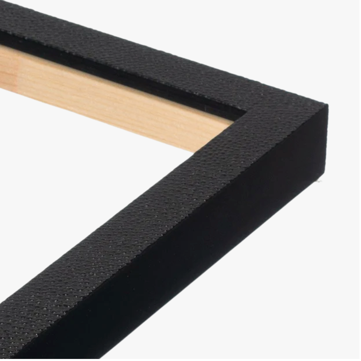 Close-up of a black textured picture frame corner with a visible wooden inner edge. The minimalist design conveys a modern and sleek aesthetic.