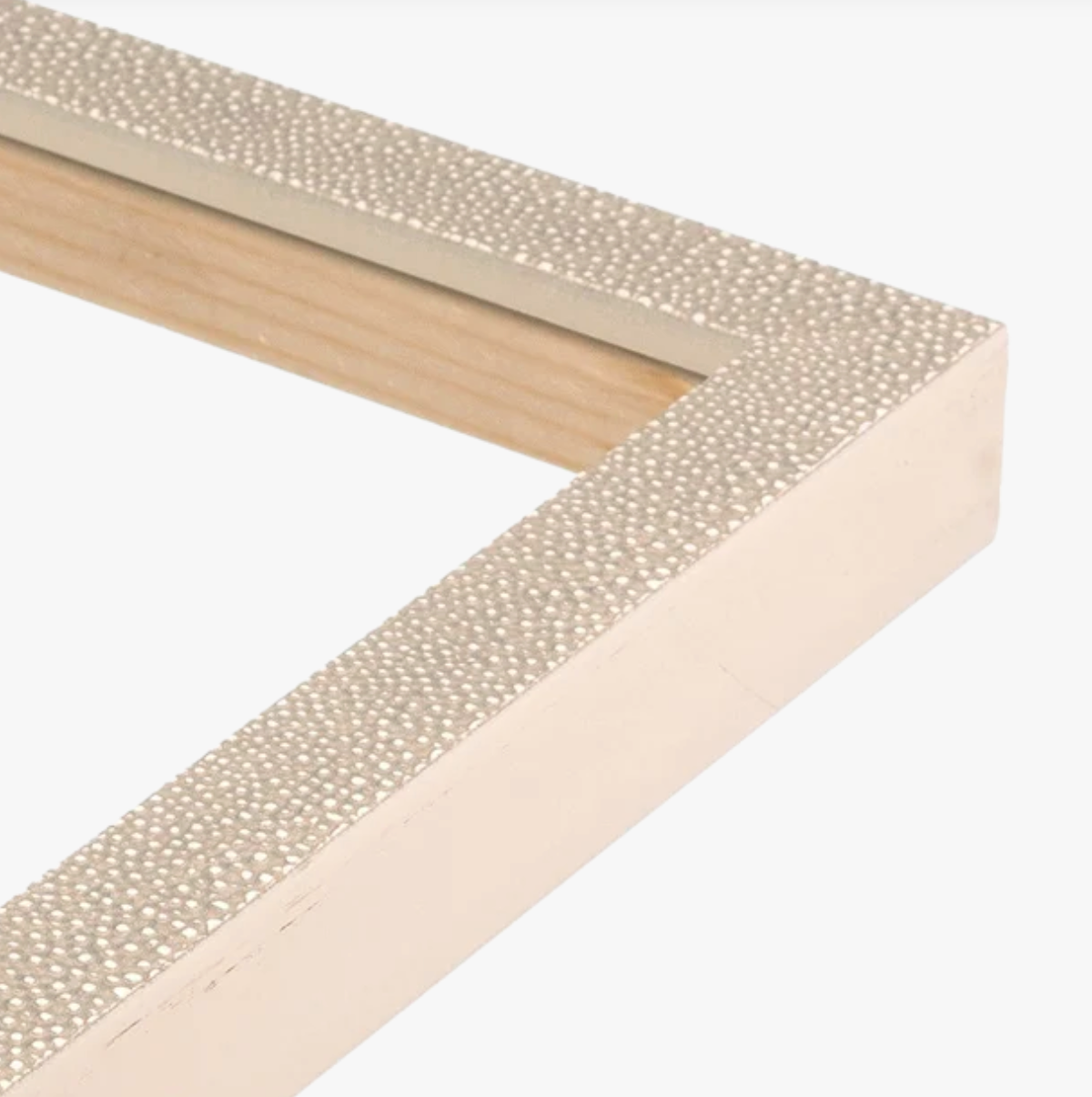 Close-up of a picture frame corner with a textured, pearl-like surface and a light wooden interior. The frame has an elegant and modern look.