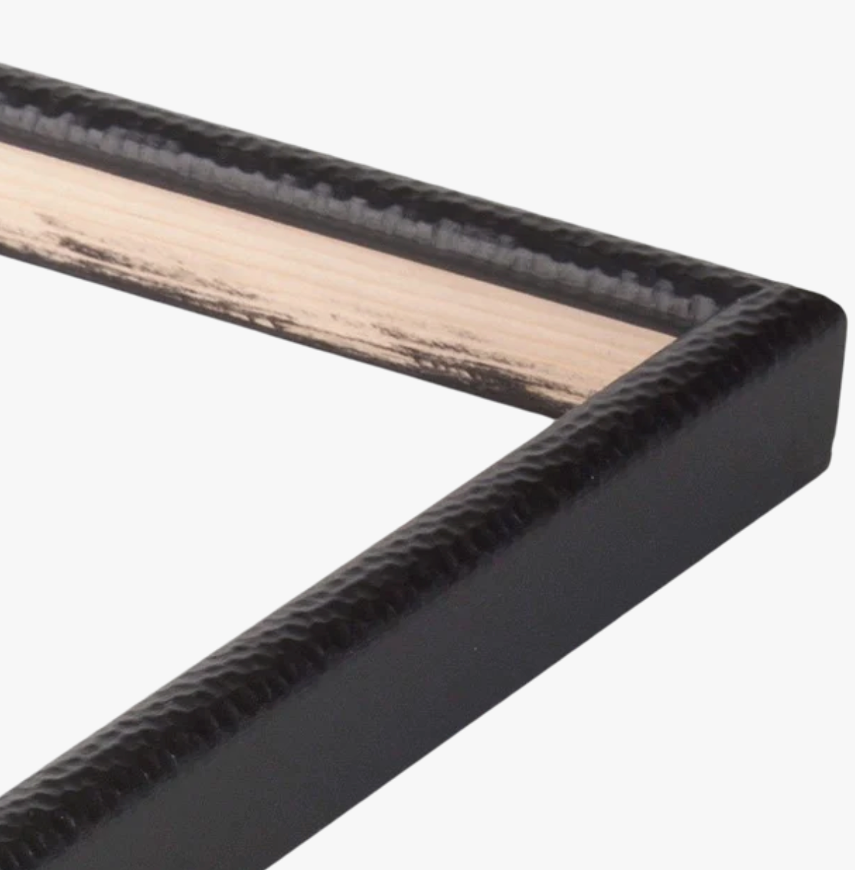 Close-up of a textured black picture frame corner against a white background. The frame has a glossy surface and light wooden accent inside.