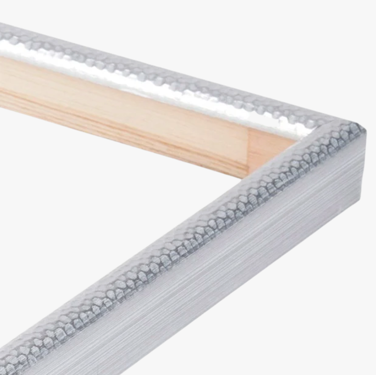 Close-up of a silver metallic picture frame corner with a hammered texture and exposed wooden interior. The frame lies on a plain white background.
