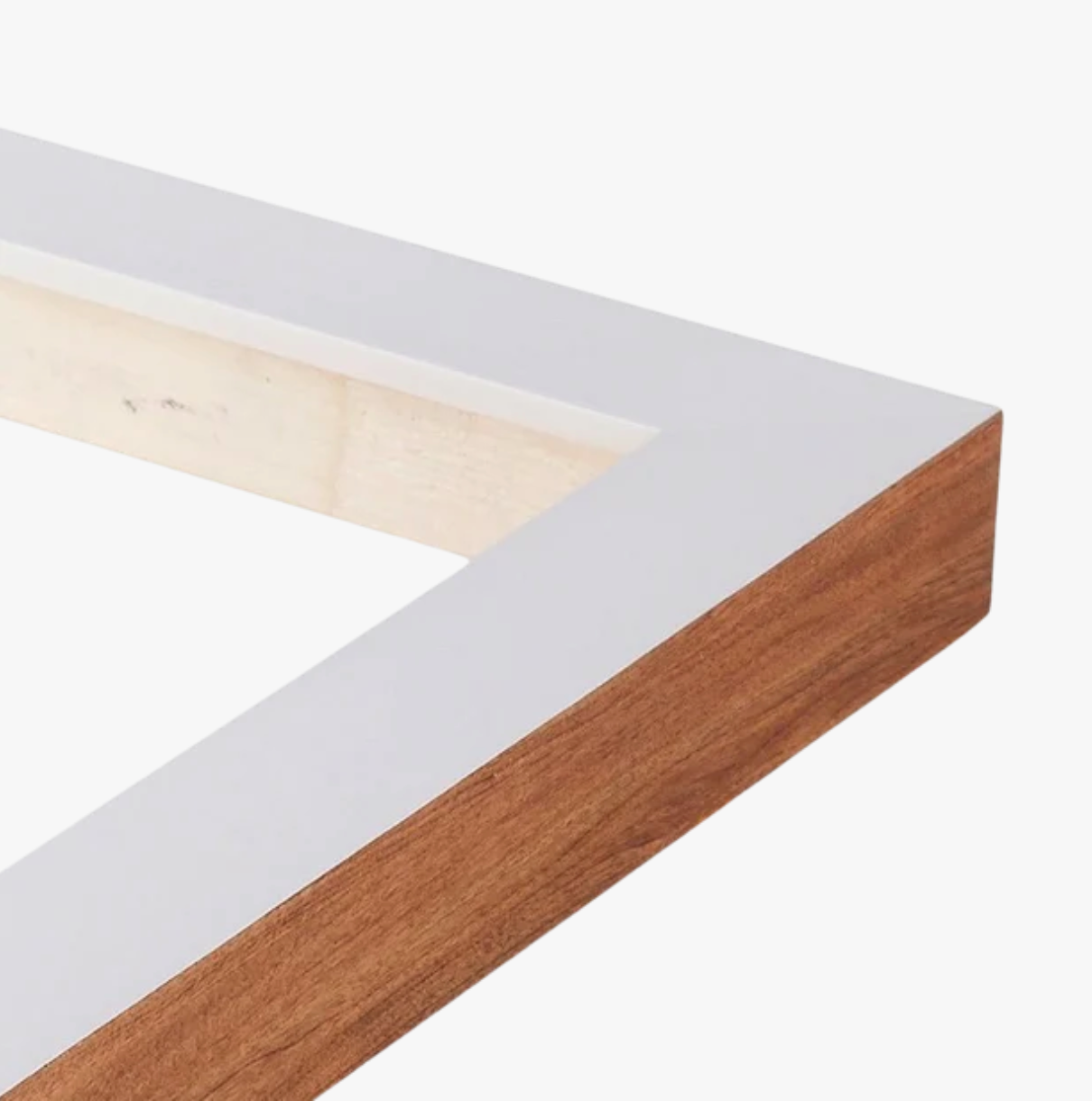 Close-up of a wooden picture frame corner, featuring white on top and natural wood on the side. The clean lines give it a modern, minimalist look.