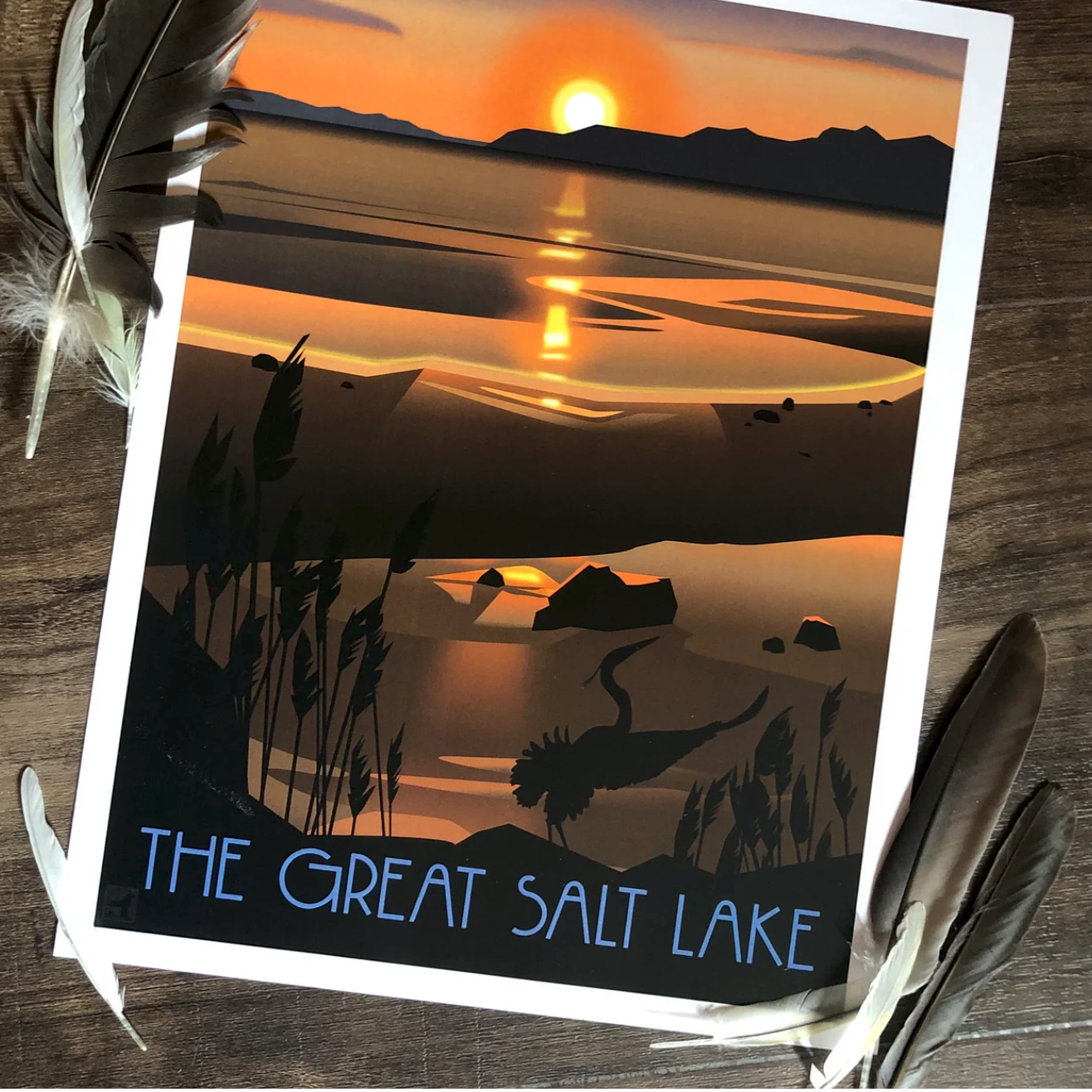 Vintage-style poster of a sunset over the Great Salt Lake, with vibrant orange and black hues, silhouettes of reeds, and calm water. Feathers frame the image.