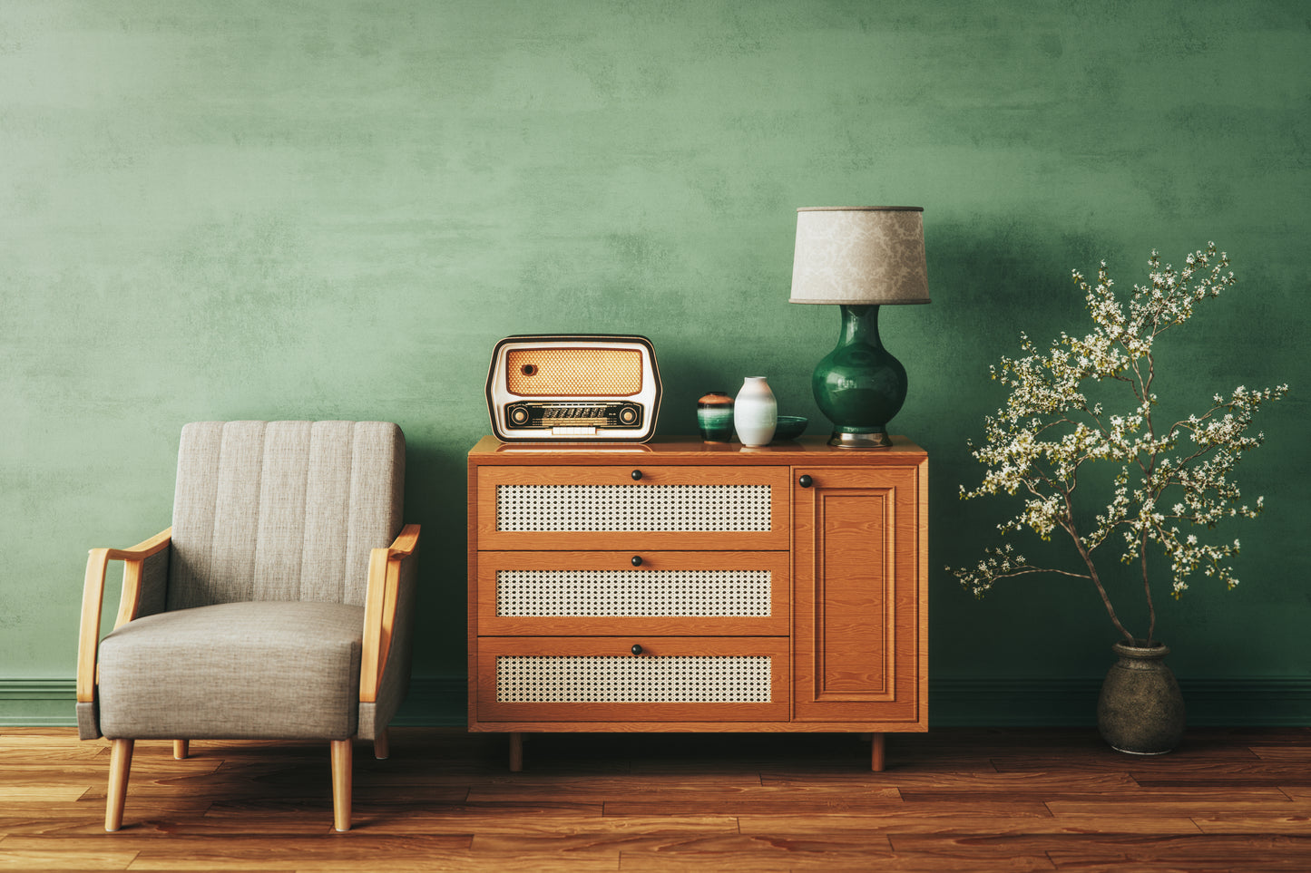A retro living room with a wooden armchair, vintage radio on a cabinet, and a green lamp. Blossoming branches in a vase against a green wall.