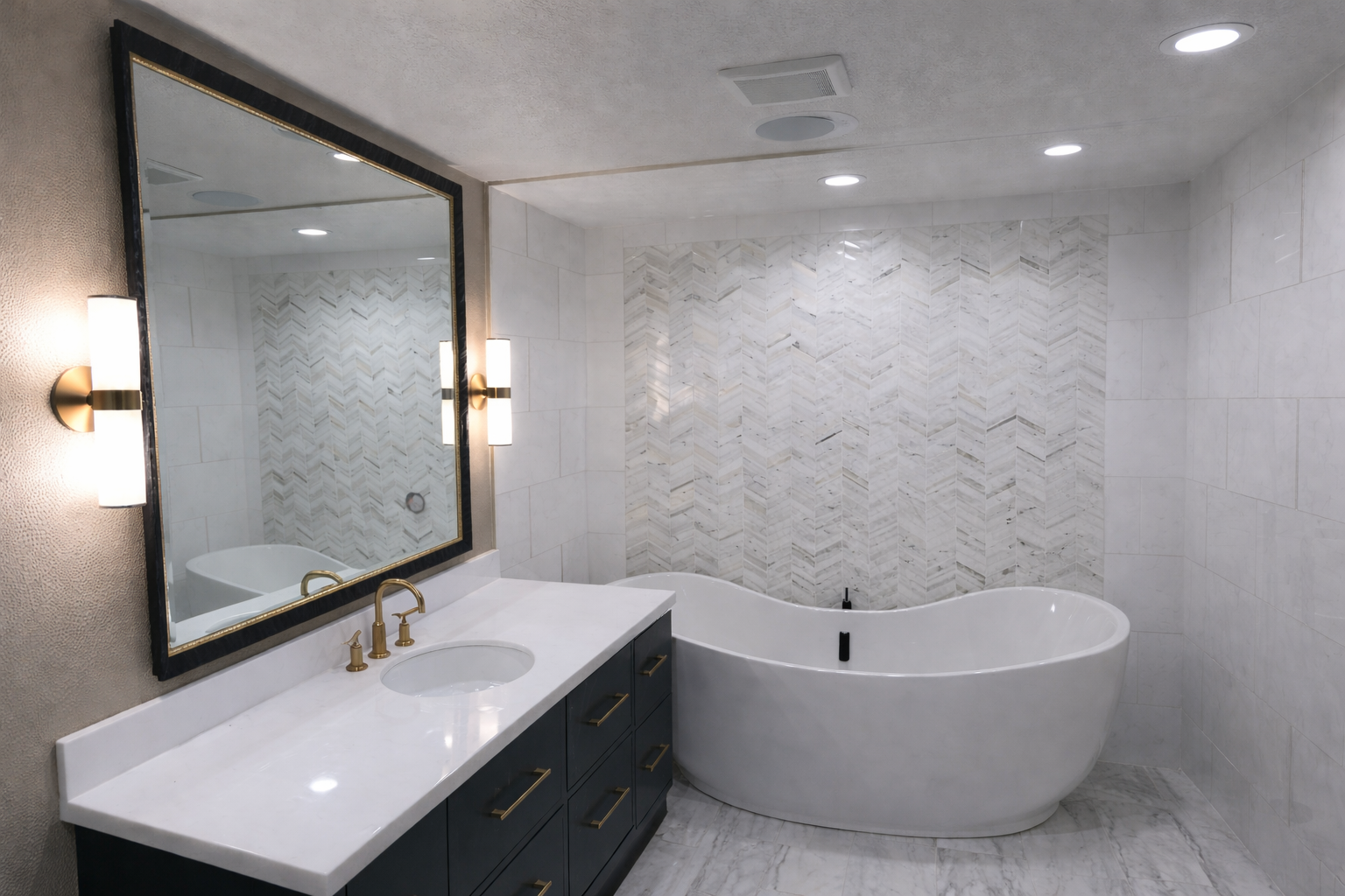 Luxury bathroom featuring a white soaking tub, dark blue vanity with gold hardware, and a marble chevron tile accent wall.