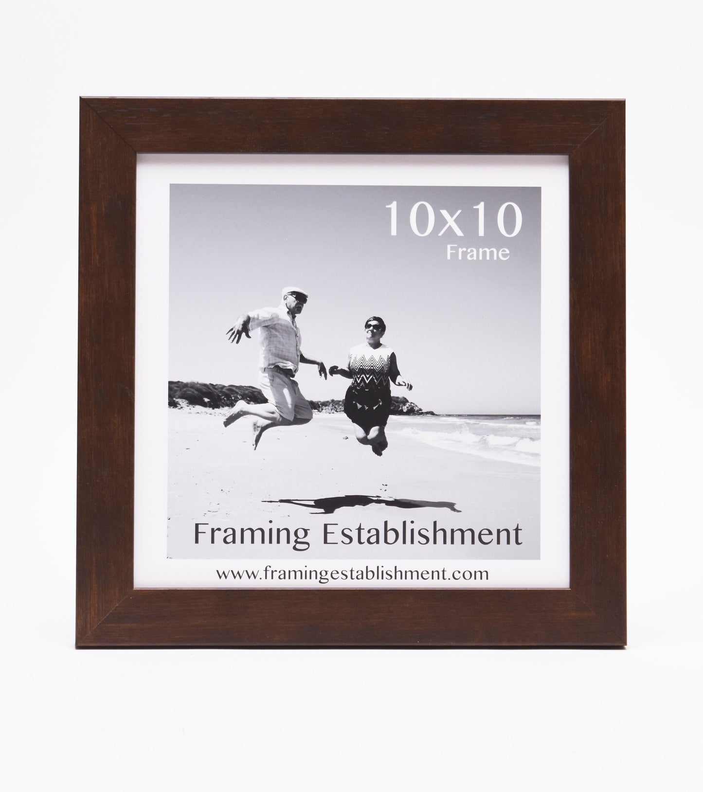 Framed black and white photo of a joyful couple jumping on a beach. The frame is labeled "10x10" and "Framing Establishment" with a web address.