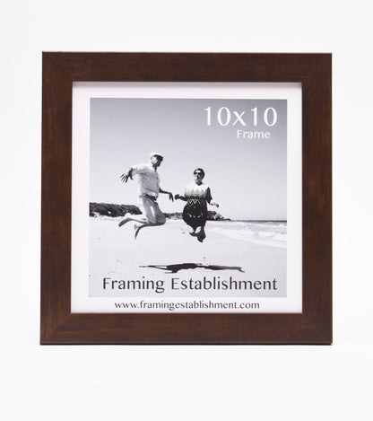 Framed black and white photo of a joyful couple jumping on a beach. The frame is labeled "10x10" and "Framing Establishment" with a web address.