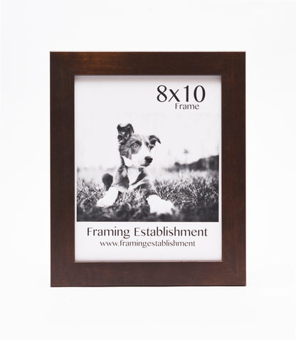 A brown wooden frame displays a black-and-white photo of a puppy lying in grass. The text reads "8x10 Frame" above and “Framing Establishment” below.