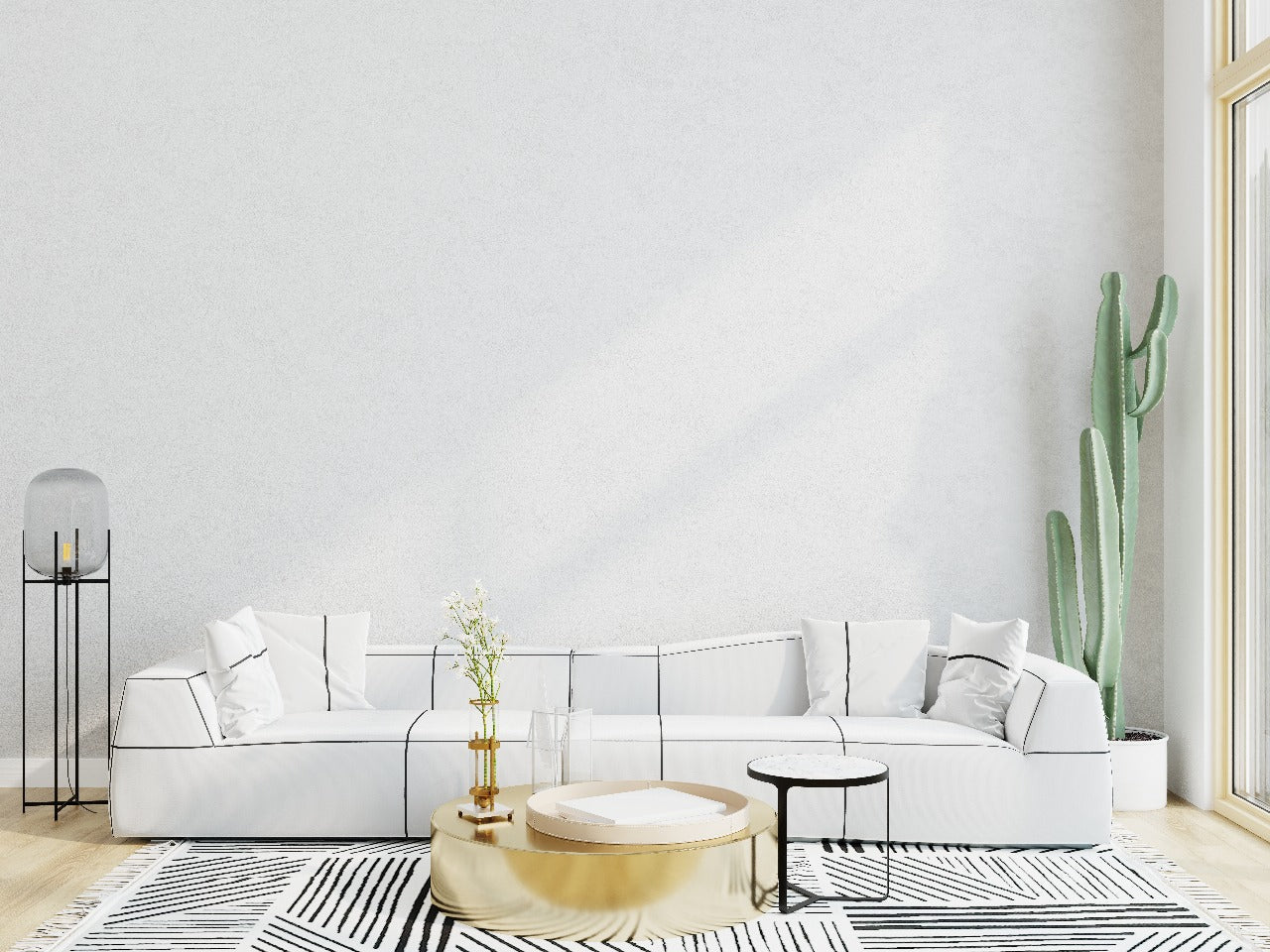 Minimalist living room with a white sofa, black-and-white patterned rug, gold and black coffee tables, a large cactus plant, and a modern floor lamp.