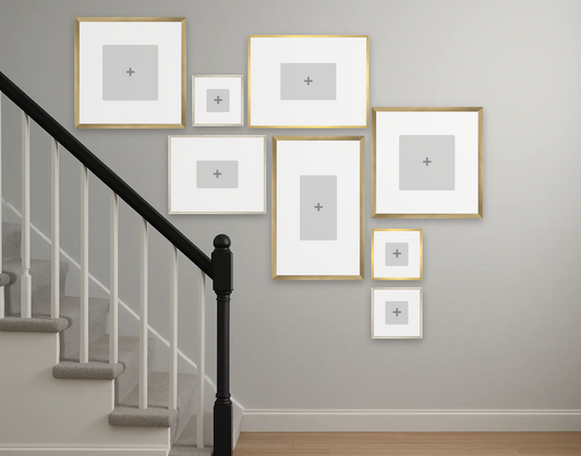 Collage of gold-framed pictures on a gray wall beside a staircase with black railing, creating a modern, artistic and balanced display.