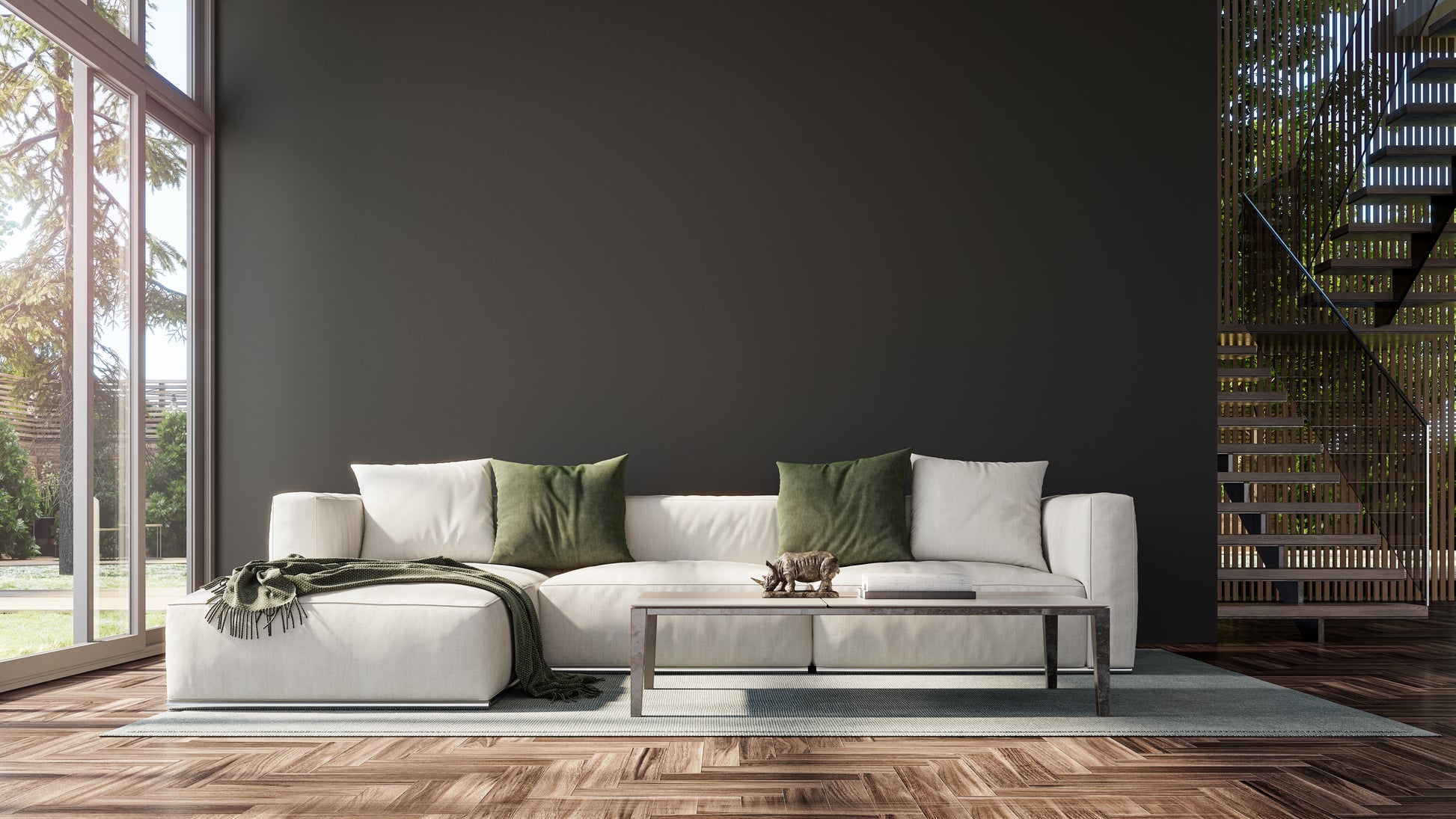 Stylish living room with a white sectional sofa adorned with green pillows and a throw. A modern coffee table displays a small sculpture, beside a staircase. Sunlight streams through large windows, casting a warm and inviting ambiance.