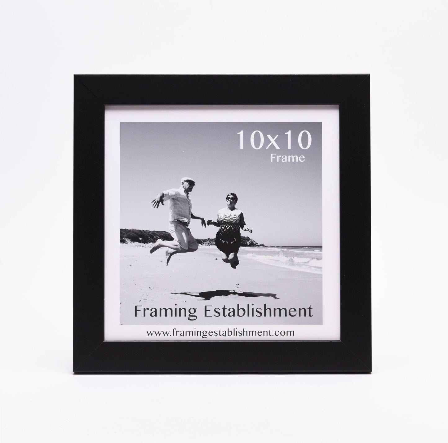 Black frame around a black-and-white photo of a man and woman joyfully jumping on a beach. "10x10 Frame" text and "Framing Establishment" logo visible.