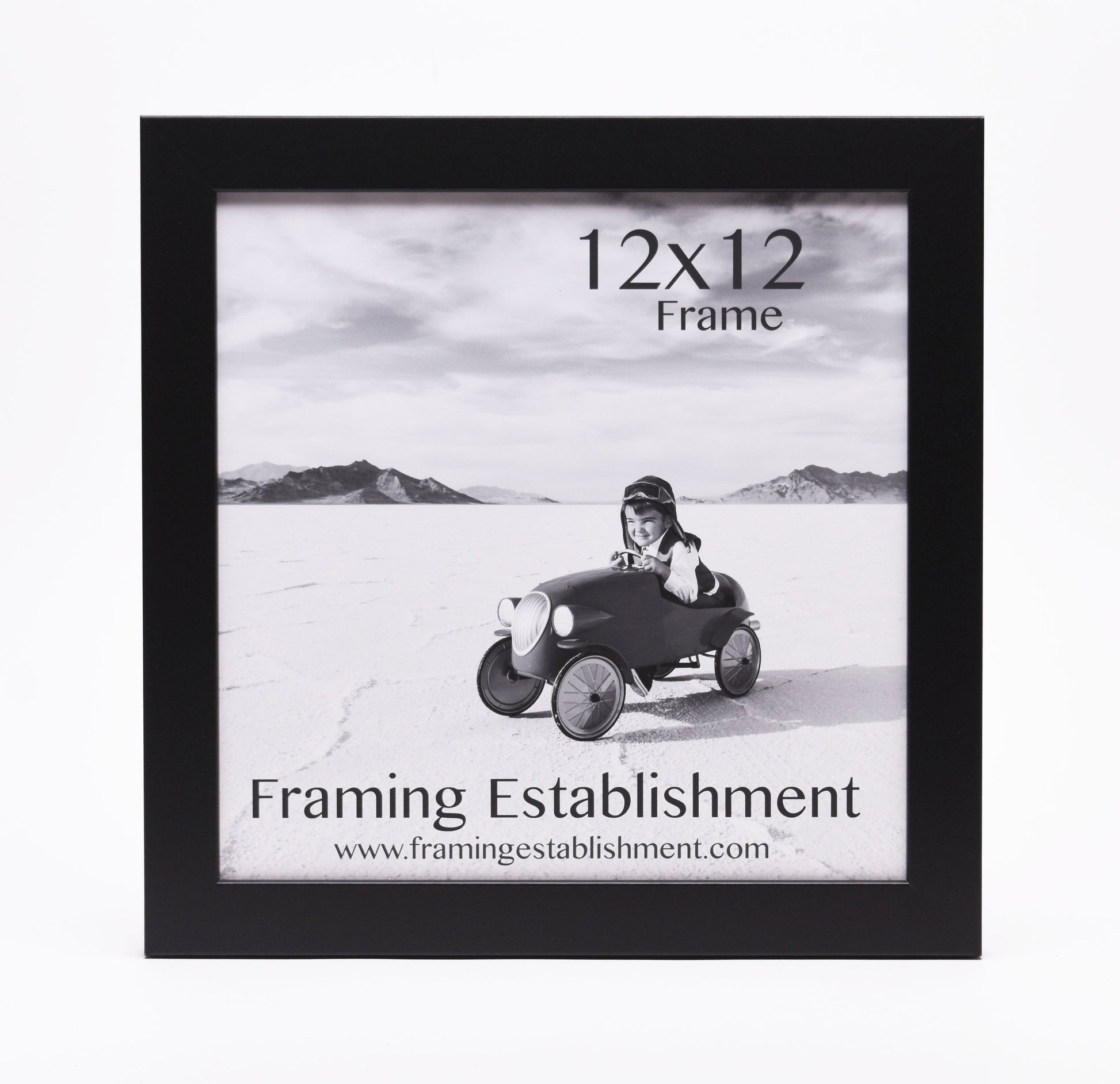 Black frame displaying a black-and-white photo of a smiling child in a toy car on a vast, flat landscape. Text: "12x12 Frame, Framing Establishment."