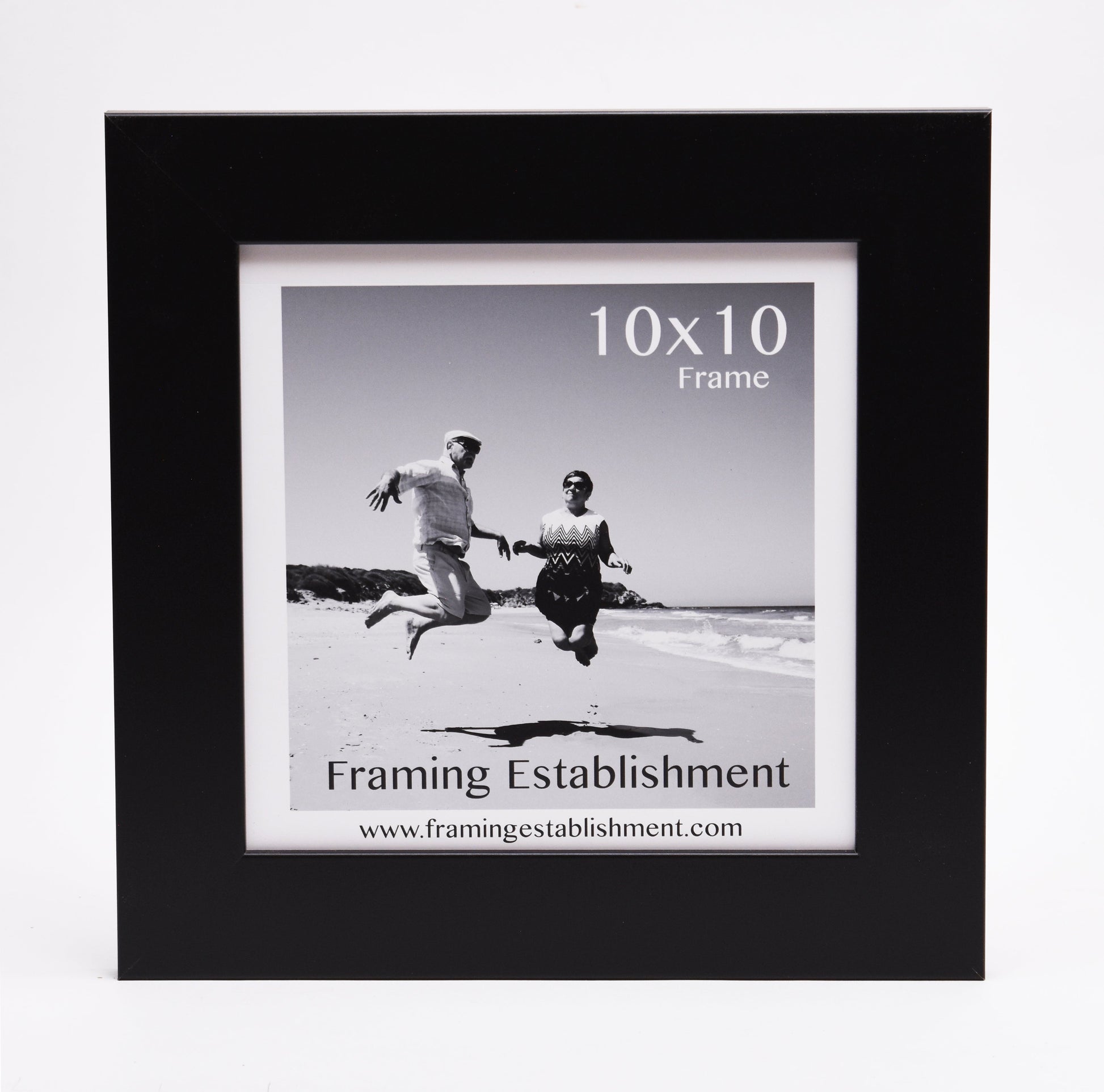 Black frame featuring a black and white photo of two people joyfully jumping on a beach, under a clear sky. Text reads "10x10 Frame" and "Framing Establishment."