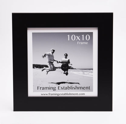 Black frame featuring a black and white photo of two people joyfully jumping on a beach, under a clear sky. Text reads "10x10 Frame" and "Framing Establishment."