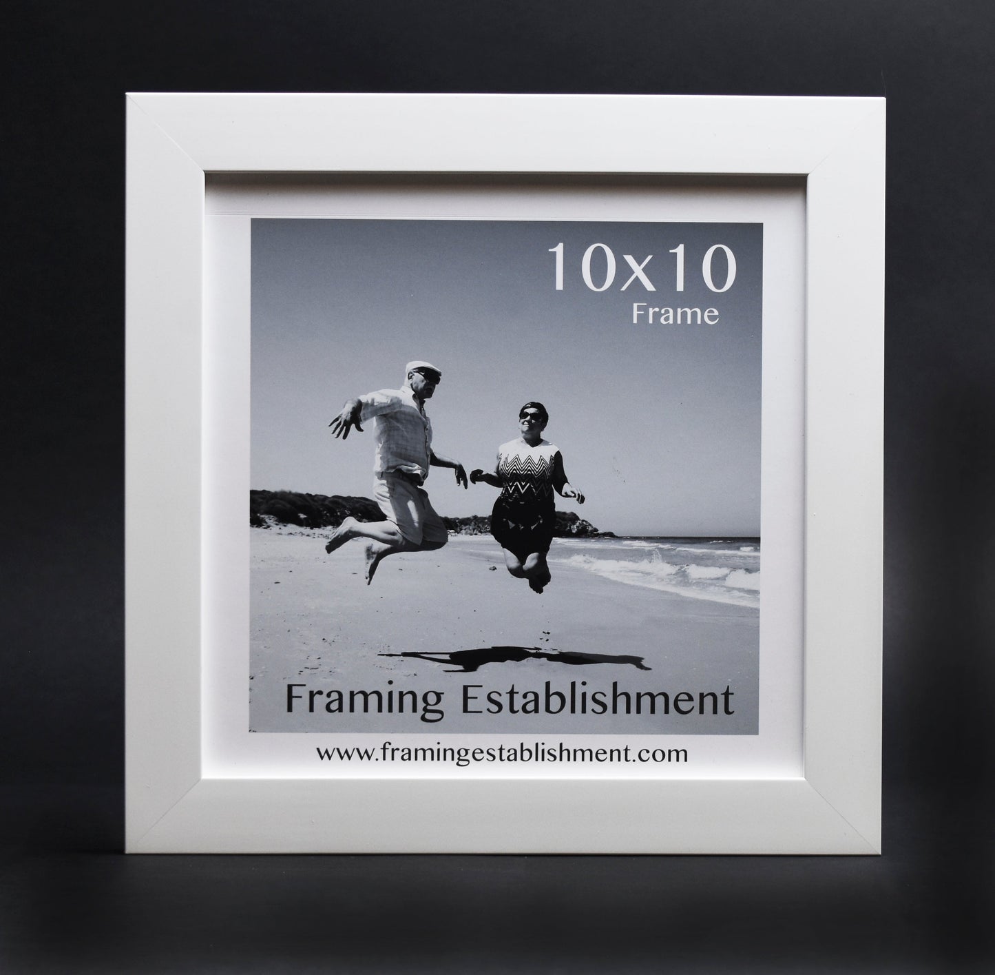 Black and white photo in a white 10x10 frame shows two people joyfully jumping on a beach, conveying a sense of freedom and happiness.