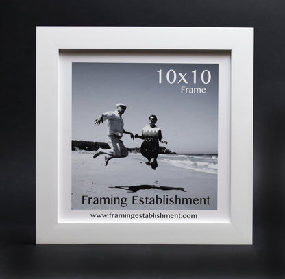 Black and white photo in a white 10x10 frame shows two people joyfully jumping on a beach, conveying a sense of freedom and happiness.