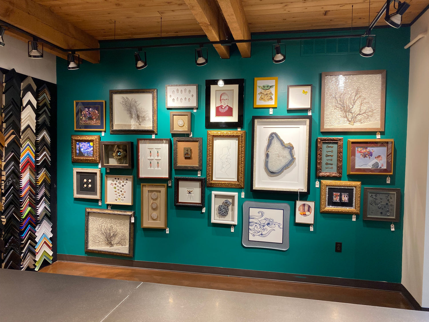 Wall with various framed pictures against a teal wall, with additional frames on a rack to the right.