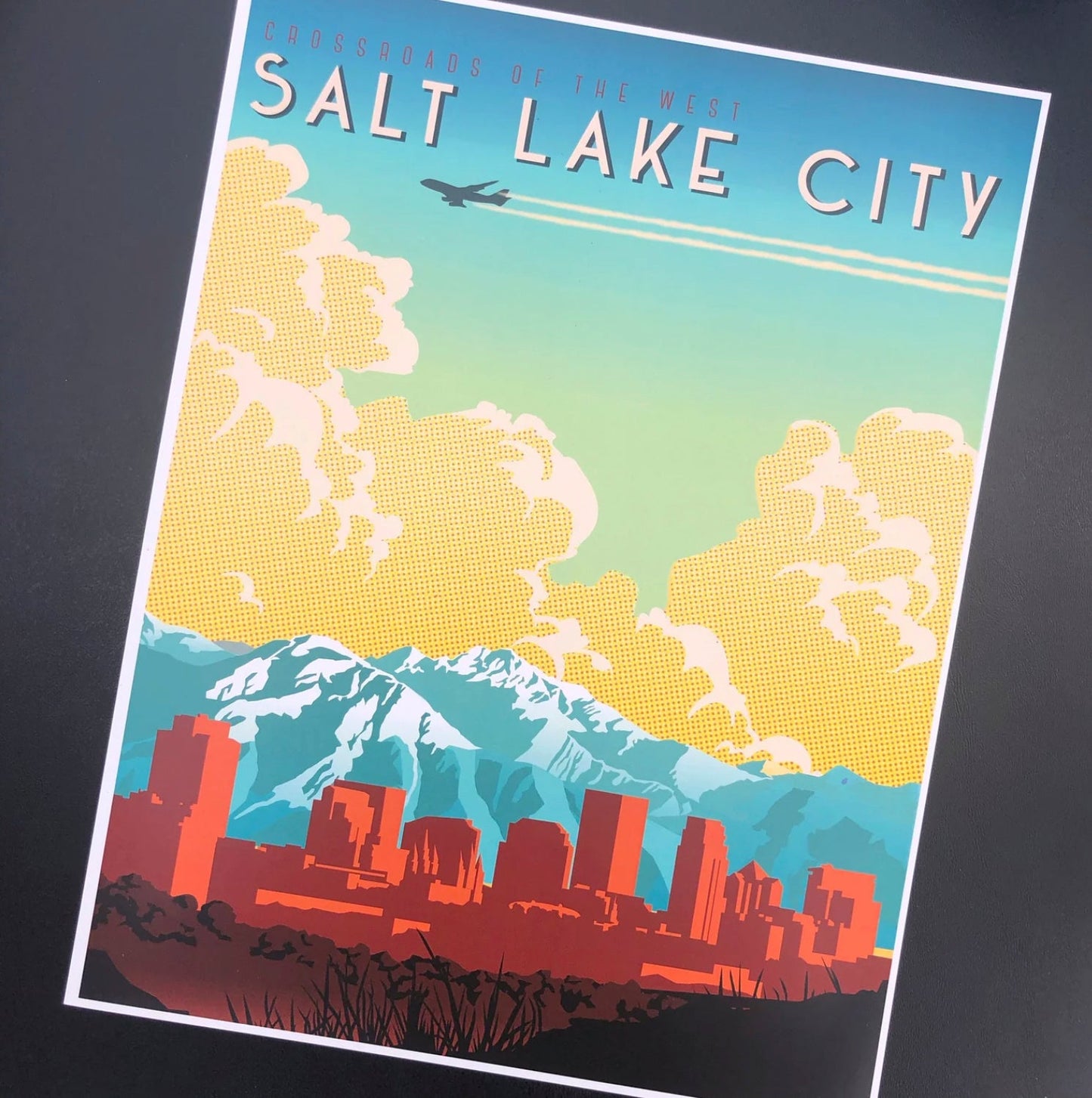 Retro-style poster of Salt Lake City, featuring a colorful skyline against mountains and clouds. An airplane flies above, conveying travel and nostalgia.