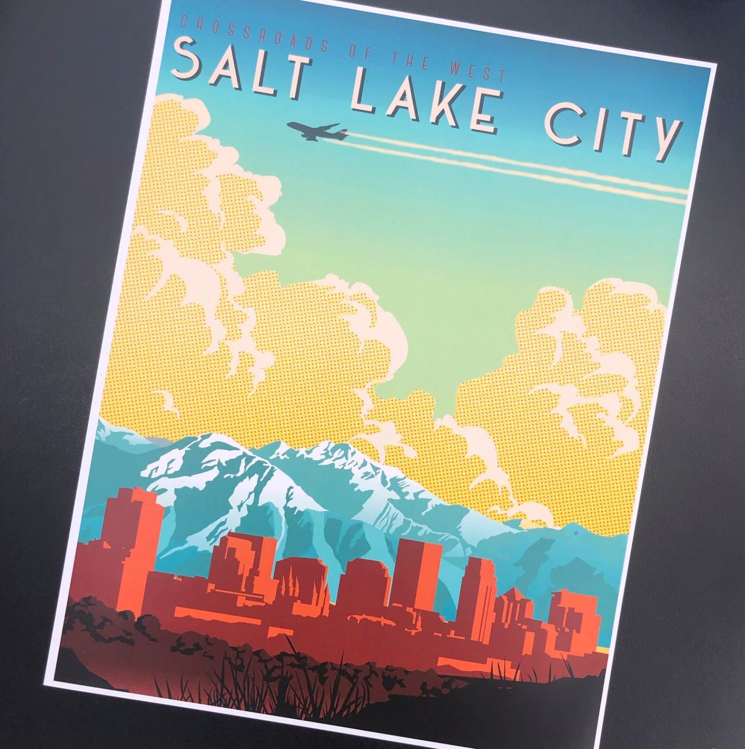Retro-style poster of Salt Lake City, featuring a colorful skyline against mountains and clouds. An airplane flies above, conveying travel and nostalgia.