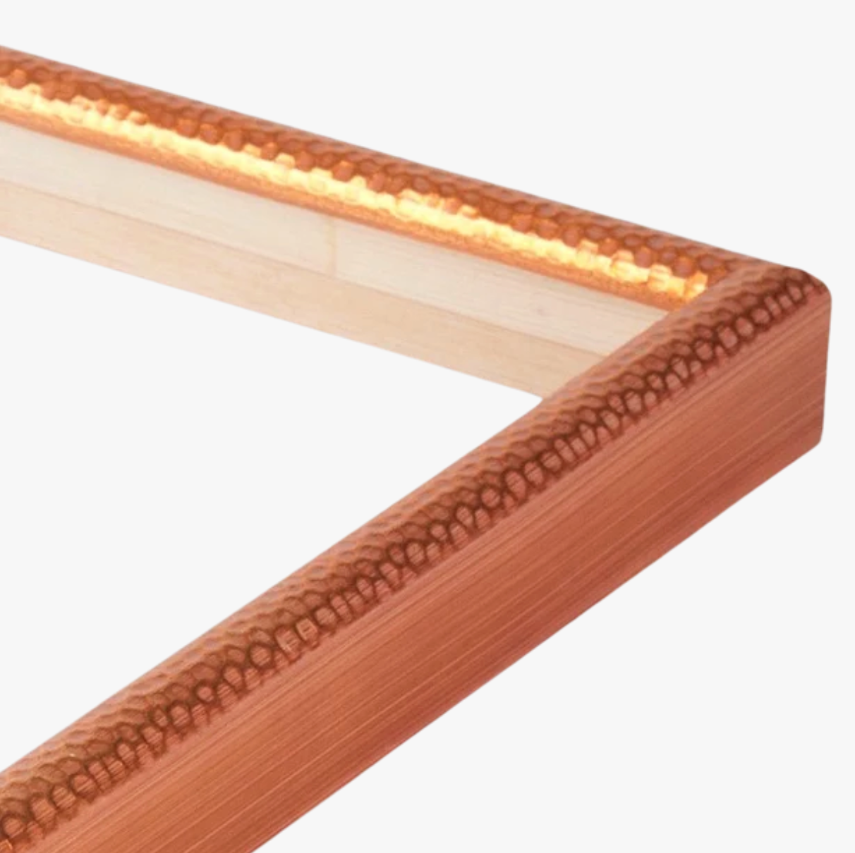 Close-up of a corner of a picture frame with a textured copper finish. The shiny surface and warm tone contrast with the light wood inside.