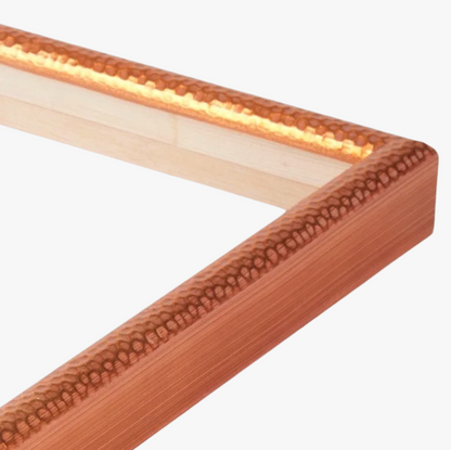 Close-up of a corner of a picture frame with a textured copper finish. The shiny surface and warm tone contrast with the light wood inside.
