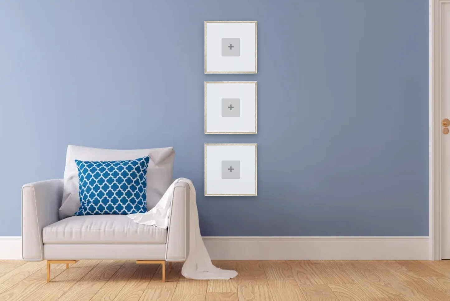 White armchair with a blue pillow against a light blue wall with three framed pictures.