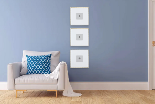 White armchair with a blue pillow against a light blue wall with three framed pictures.