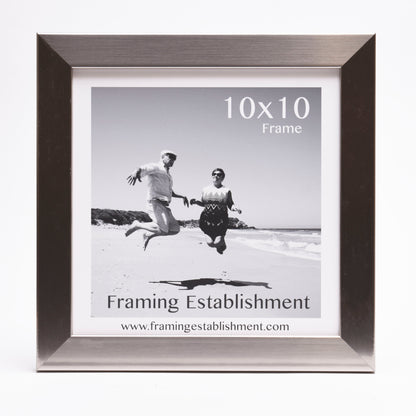 Black and white photo of a joyful couple jumping on a sunny beach. They are framed in a stylish silver 10x10 frame from Framing Establishment.
