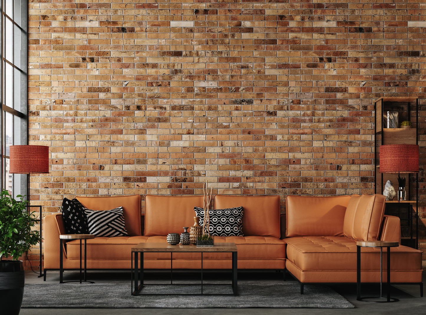 Stylish living room with a brown leather sectional sofa against a rustic brick wall. Features geometric pillows, modern tables, and red lamps, exuding a warm, contemporary vibe.