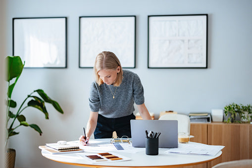 Woman working at a desk with a laptop and documents in a modern office setting.