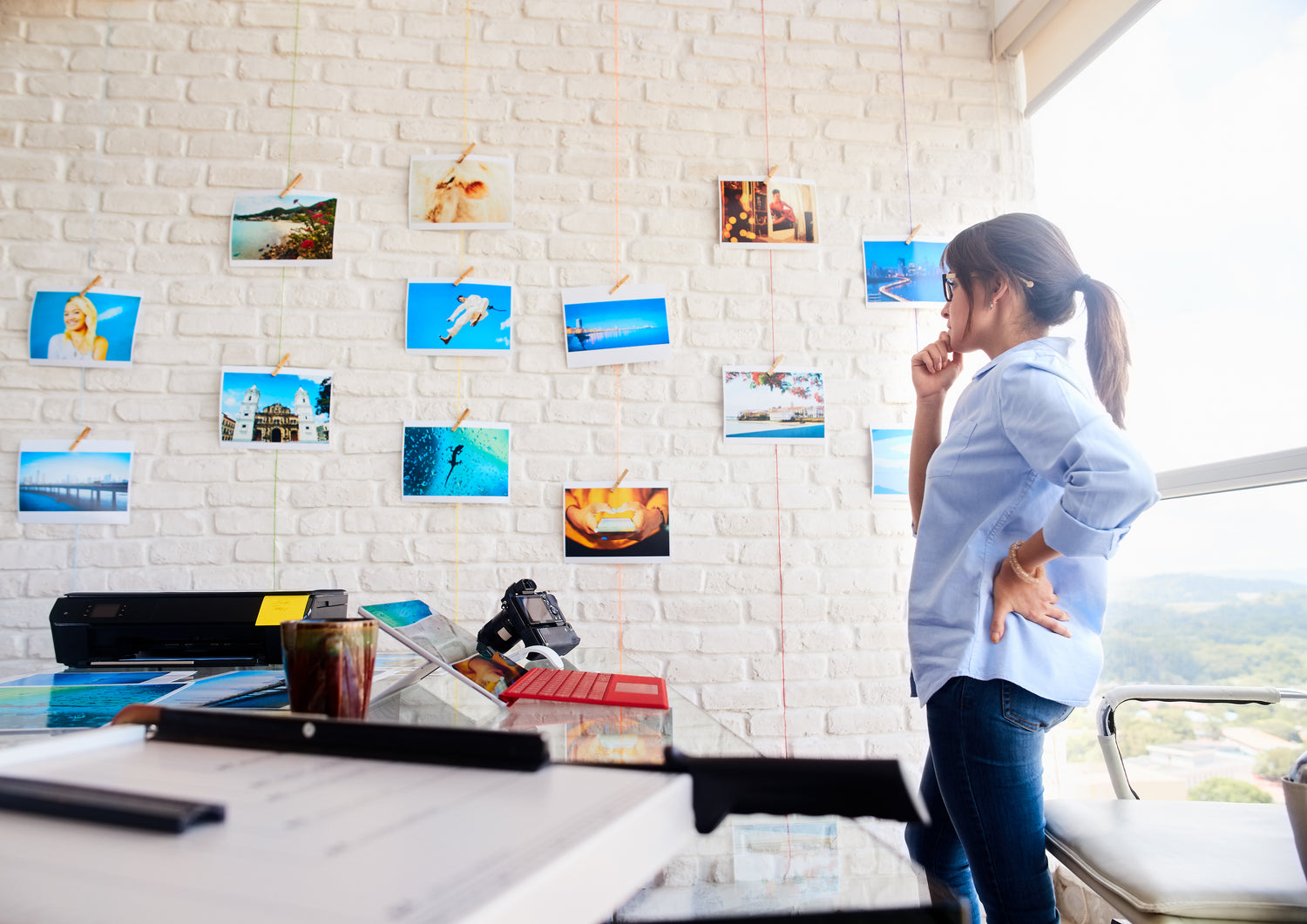 Woman standing in a room with photos pinned to a white brick wall.